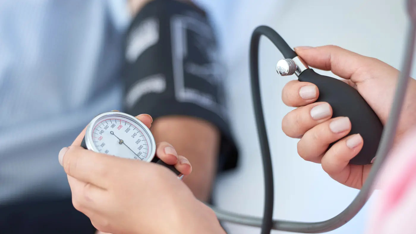 Close-up of hands operating a manual blood pressure gauge and inflating a cuff on a patient's arm during a blood pressure reading