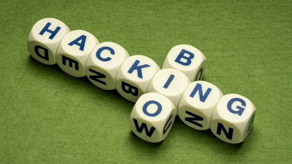 White letter dice arranged in a crossword pattern spelling out HACKING and BIOWING on a green felt surface, representing the concept of biohacking
