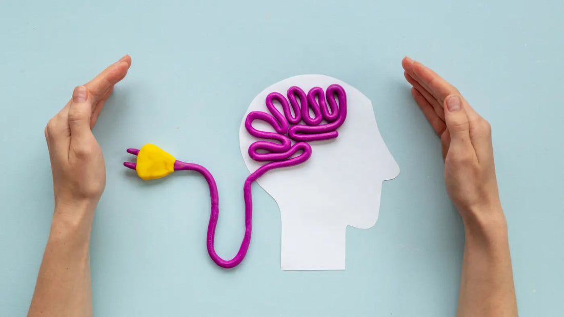 Creative concept image of a white paper head cutout on a light blue background, with a purple clay brain connected by a cord to a yellow electrical plug, framed by two cupped hands