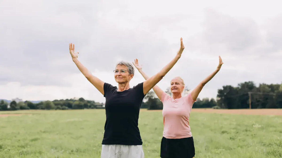 Two older women with arms raised standing in a green field outdoors, symbolising active ageing and the body's defence against free radicals