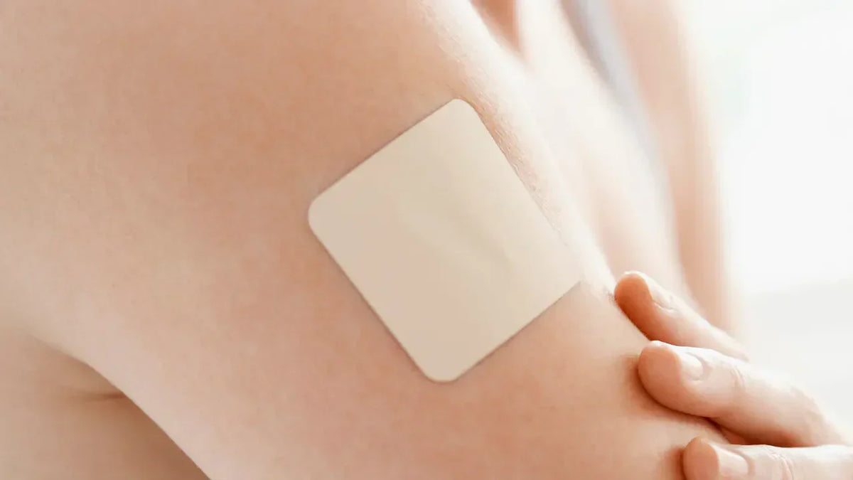 Close-up of a square beige transdermal patch applied to the skin of an upper arm, representing GLP-1 dermal patches