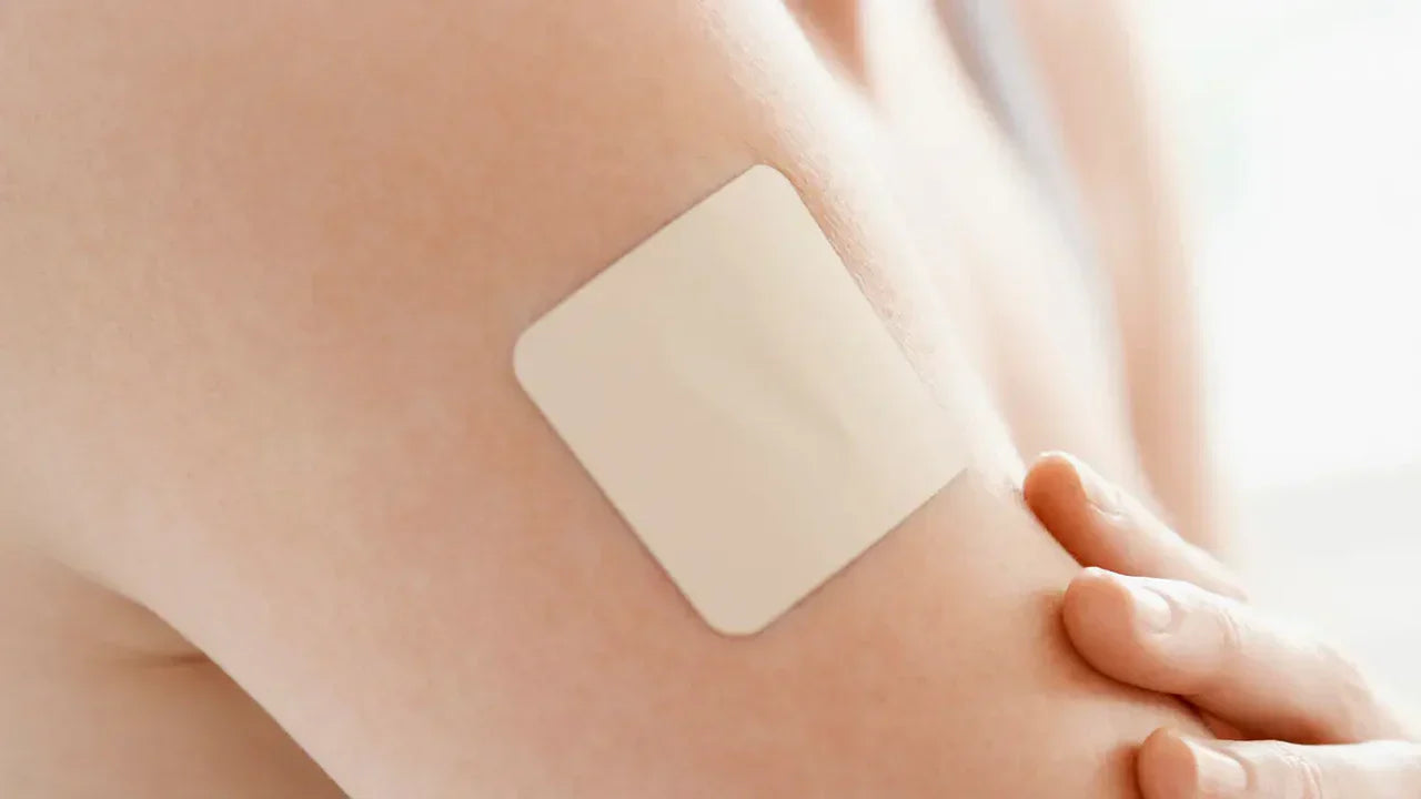 Close-up of a square beige transdermal patch applied to the skin of an upper arm, representing GLP-1 dermal patches