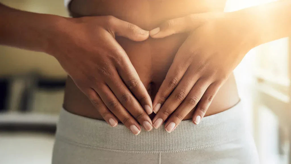 Close-up of a woman's abdomen with hands forming a heart shape over her stomach, symbolising gut health and digestive wellness