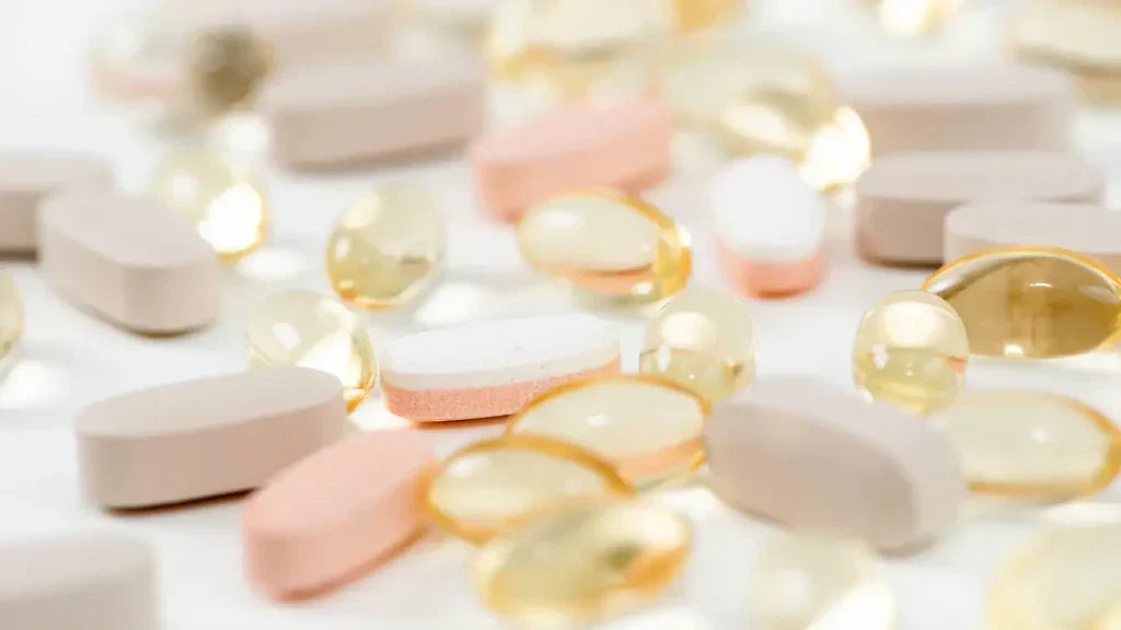 Assortment of supplement tablets and softgels – white tablets, pink tablets, and golden gel capsules – scattered on a white surface
