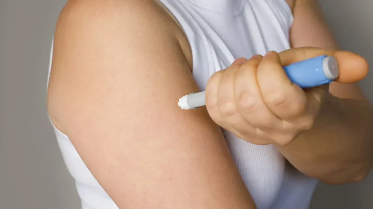 Close-up of a person self-administering a blue auto-injector pen into their upper arm, representing injectable weight management medications such as Wegovy, Ozempic, and Mounjaro