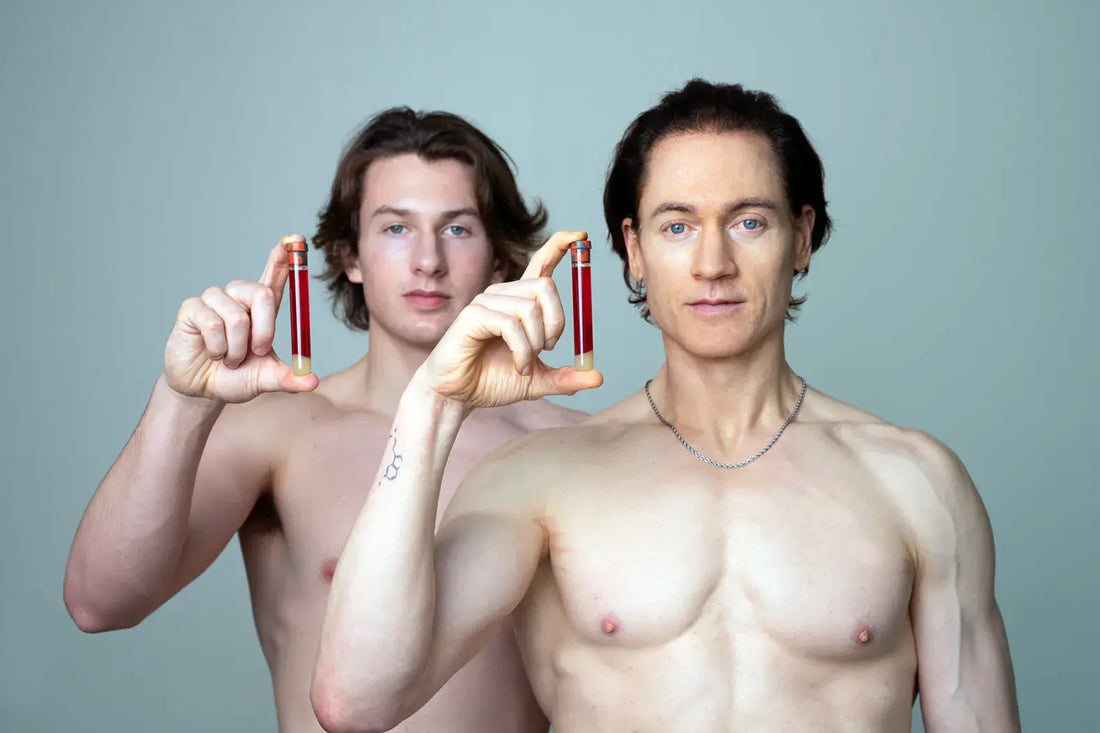 Bryan Johnson and his son each holding up a small vial of blood against a grey-green studio background, depicting their plasma exchange experiment