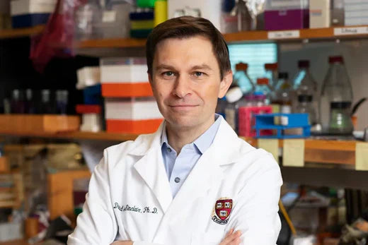 David Sinclair, Harvard longevity researcher, in a white lab coat with arms folded, standing in front of laboratory equipment and supplies