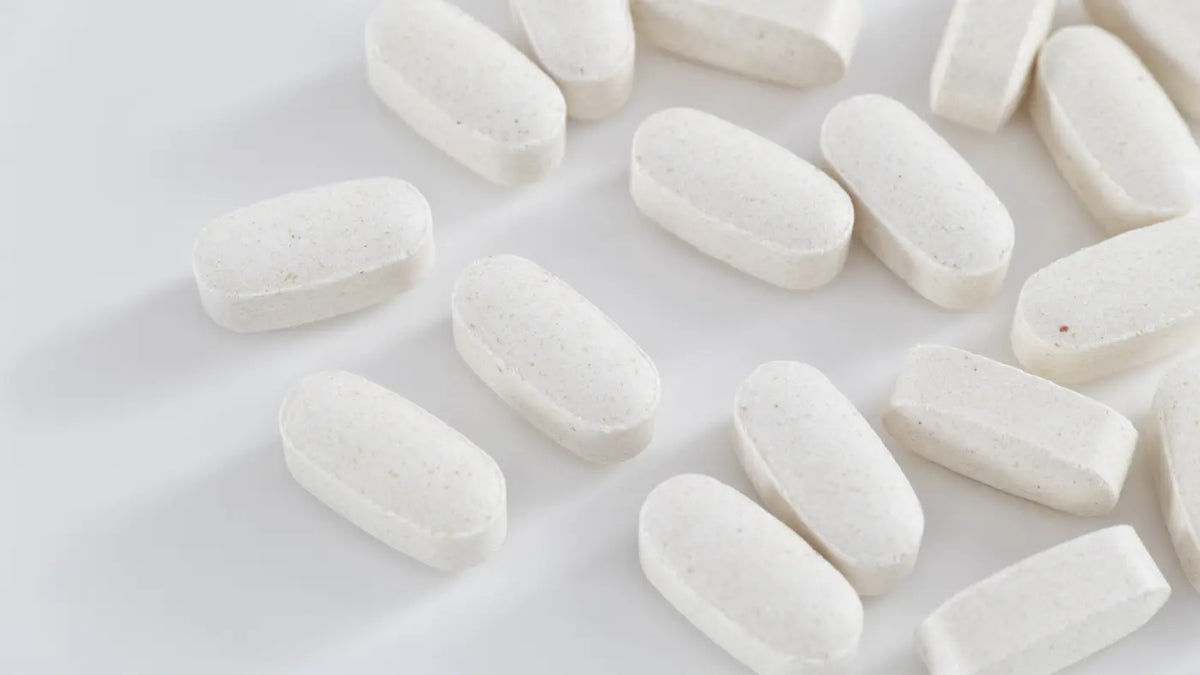 Multiple white oblong magnesium supplement tablets scattered on a clean white surface