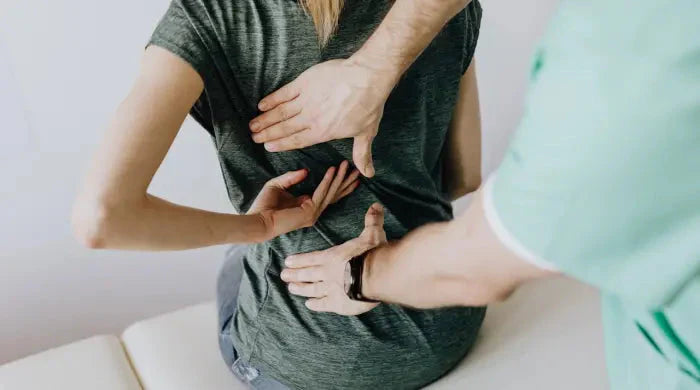 Healthcare professional pressing both hands on a seated patient's lower back during a pain assessment or physical therapy session