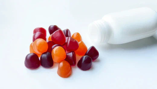 Pile of colourful red, orange and dark red gummy supplements spilled from a white bottle onto a white surface