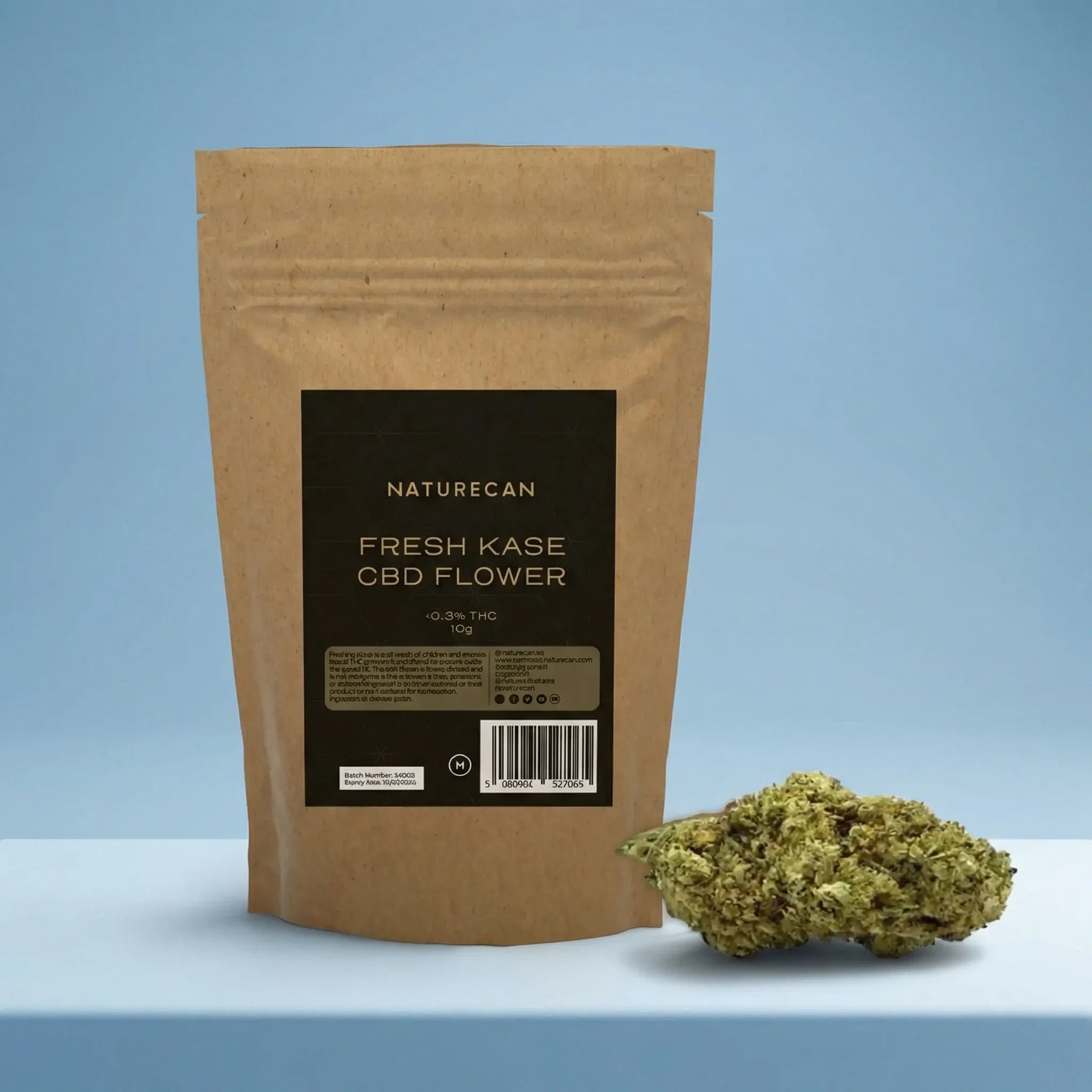 Naturecan Fresh Kase CBD Flower lifestyle – kraft paper pouch with dark label on light blue background, with CBD flower bud displayed beside it